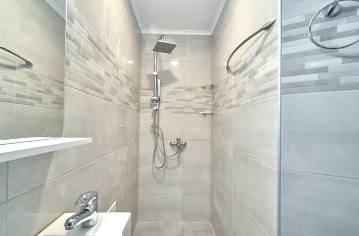 Clean, tiled bathroom interior featuring a modern walk-in rain shower fixture and sleek sink area