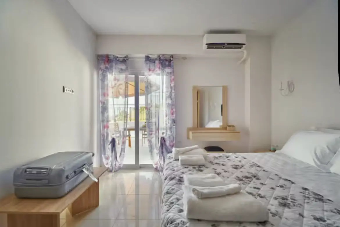 View from the side of a double bed in Suite 1, showing a vanity dresser and large sliding glass doors with floral curtains leading to the terrace