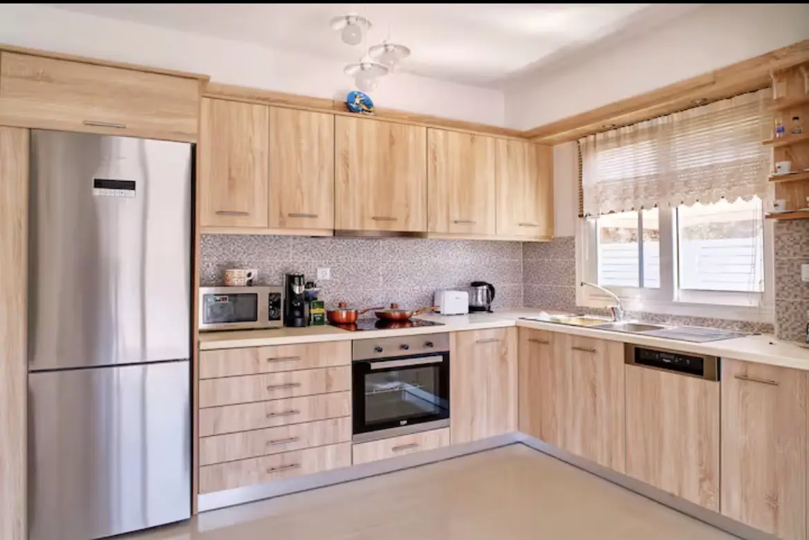 Sleek L-shaped light wood kitchen cabinets with built-in stainless steel refrigerator, oven, stove, microwave, and dishwasher in Suite 2