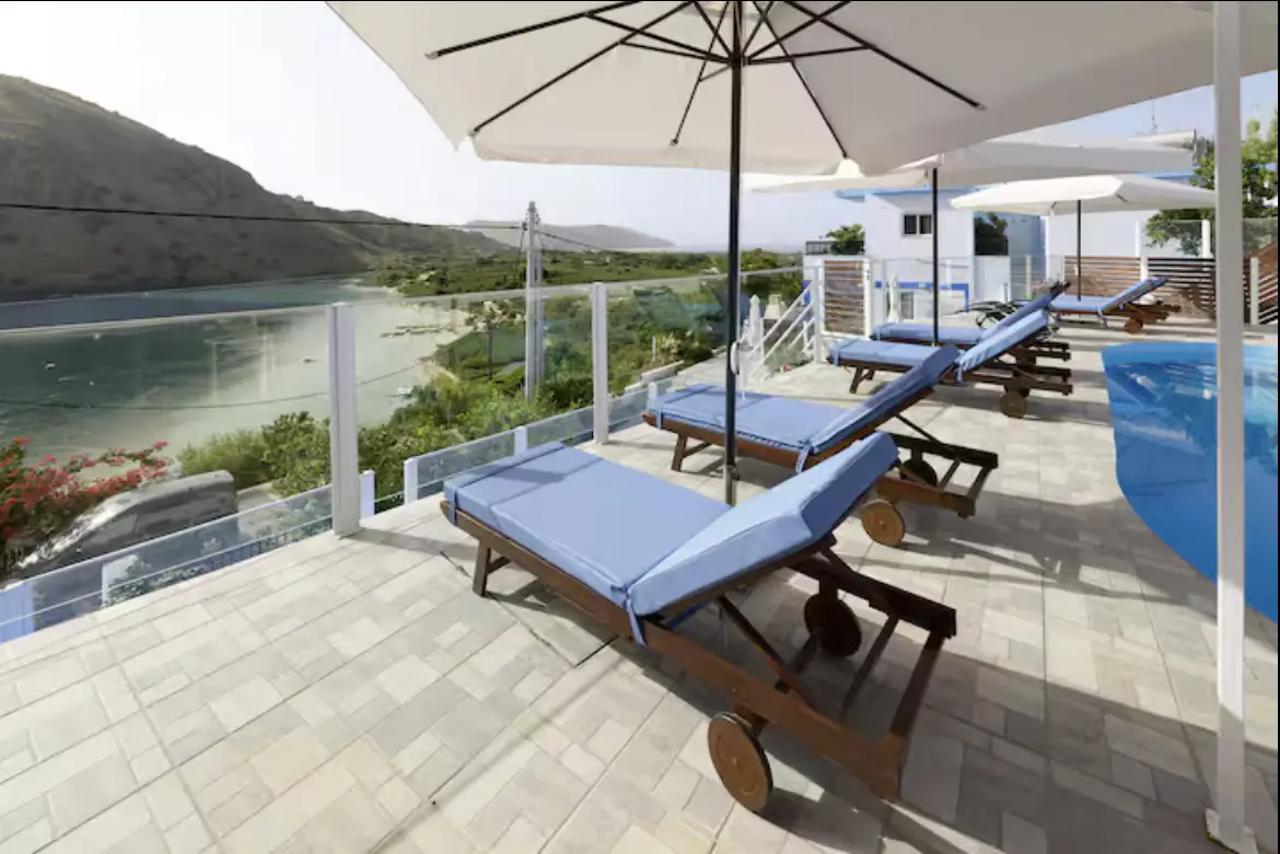 Two comfortable blue padded sun loungers under a large white patio umbrella on the stone-paved deck of Suite 2